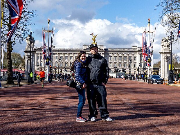 Benjamin Kott und Darina Schkolnik stehen gemeinsam auf der von britischen Flaggen gesäumten Straße vor dem Buckingham Palace in London.